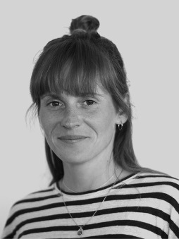 Schwarzweißes Portrait von Eva Luna Hartmann. Weibliche, lächelnde Person mit langen, dunklen Haaren.