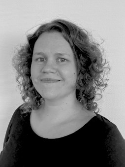 Schwarzweißes Portrait von Caroline Kluge. Weibliche Person mit lockigen Haaren, die zugewandt guckt.