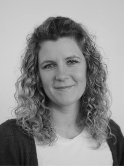 Schwarzweißes Portrait von Pia Junge-Wentrup. Weibliche, lächelnde Person mit mittellangen, lockigen Haaren.